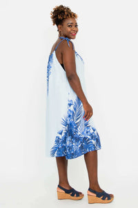 Side view of woman wearing a light blue tropical print dress with adjustable shoulder tie
