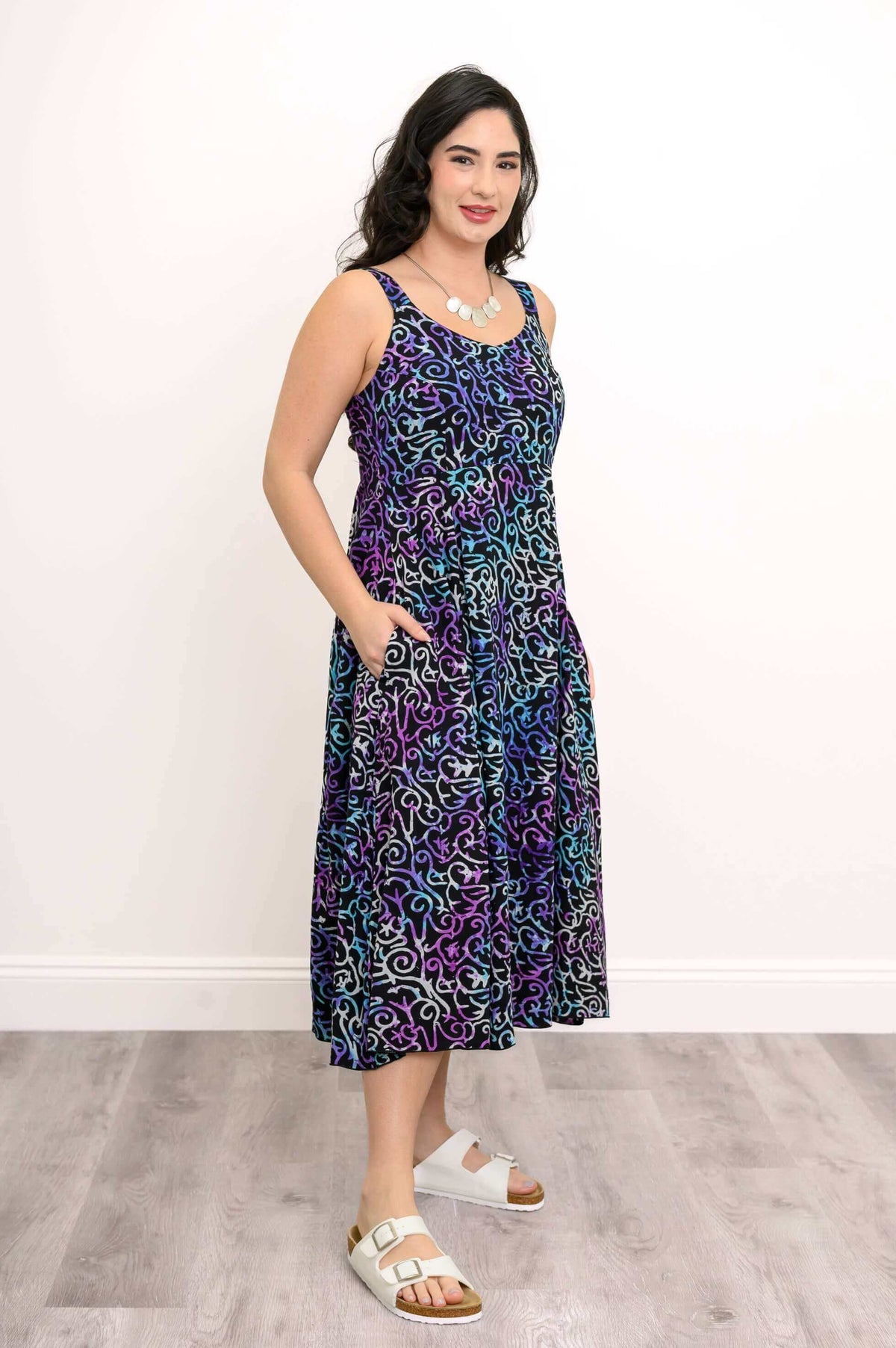 Woman displaying side view of a black dress with blue and purple swirls, hand in pocket