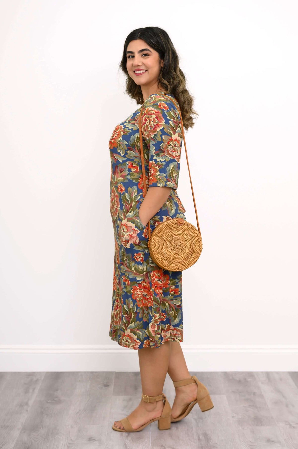Side view of a woman in a floral bamboo dress with a round woven bag