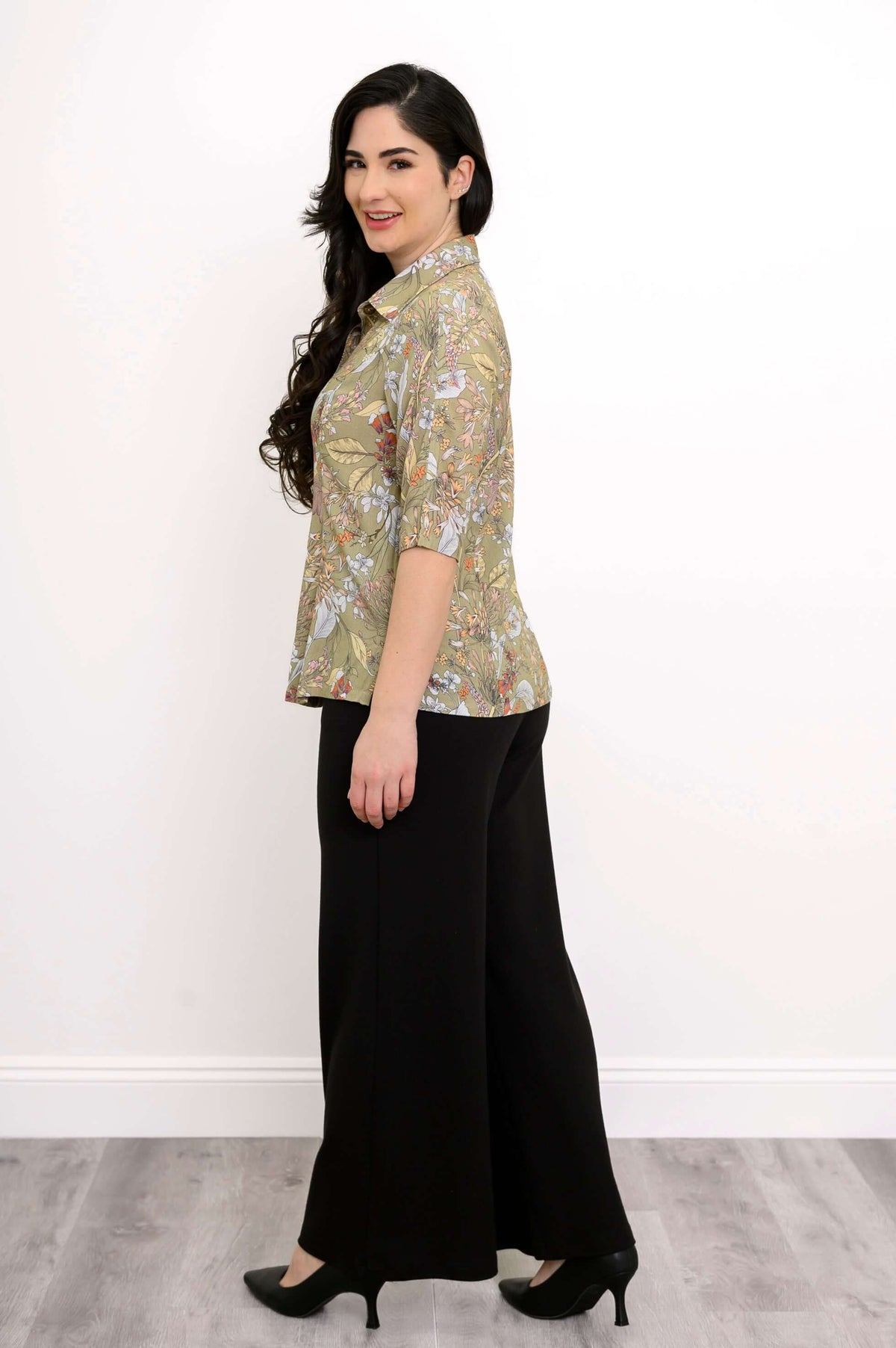 Side view of woman in a green floral blouse and black wide-leg pants