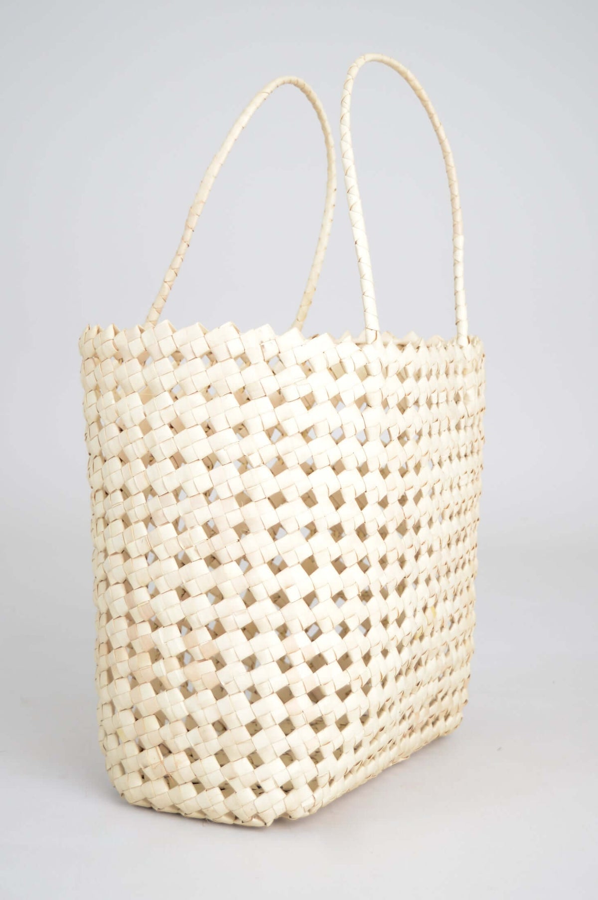 Angled side view of hand woven rattan basket with long handles