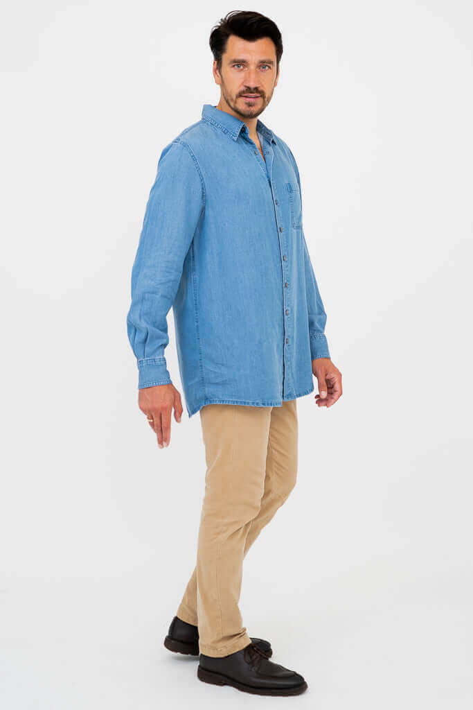 Man in side pose wearing light blue button-up shirt and tan pants