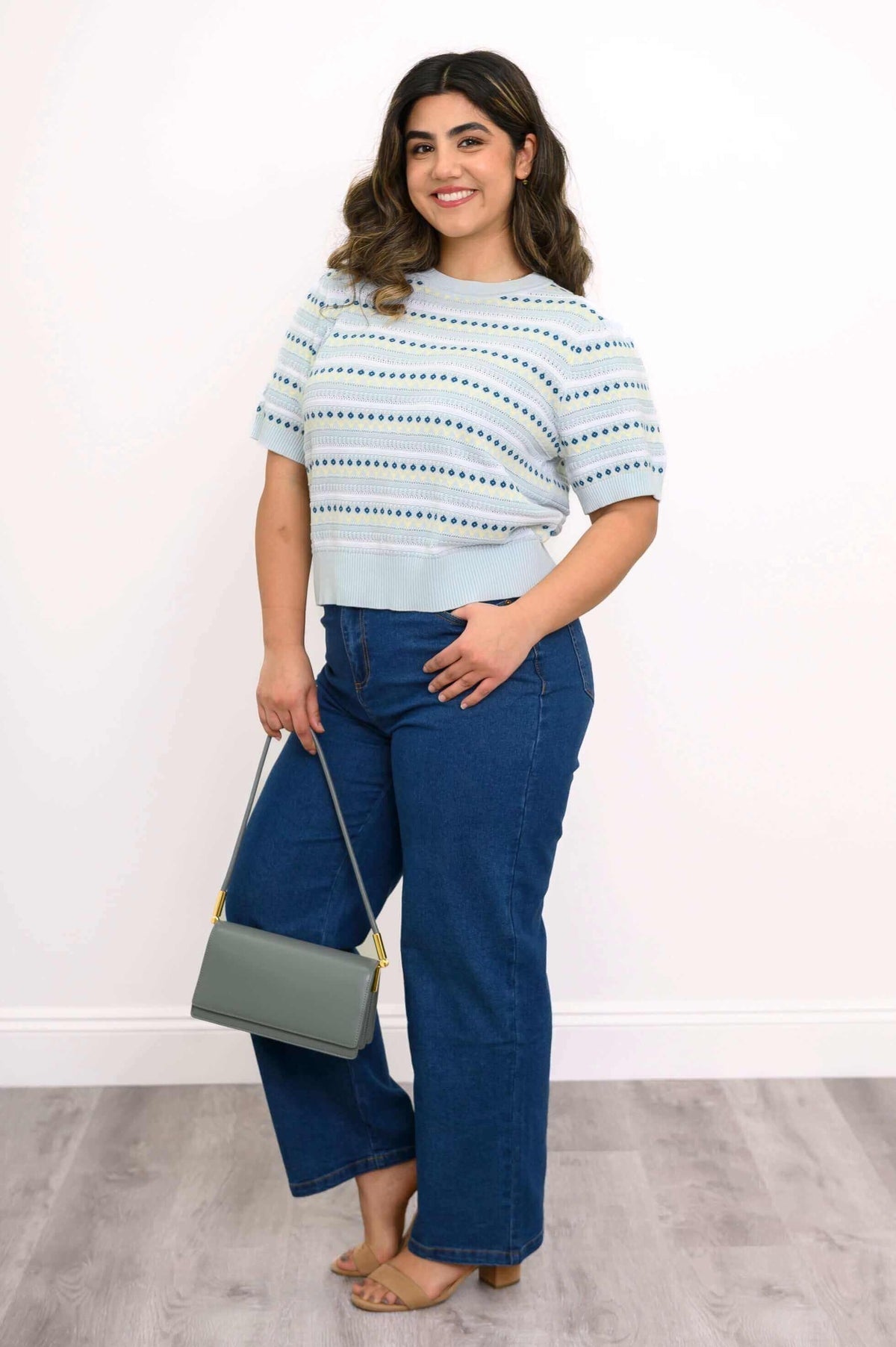 Angled view of model styling Sweater with blue jeans and gray handbag