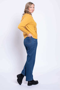 Side view of a woman in blue straight leg jeans and a yellow hoodie, hands in pocket.