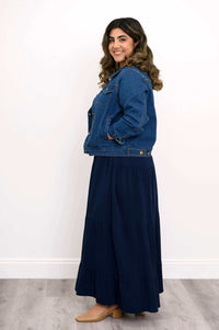 Side view of model wearing a denim jacket paired with a tiered dark blue ruffle skirt