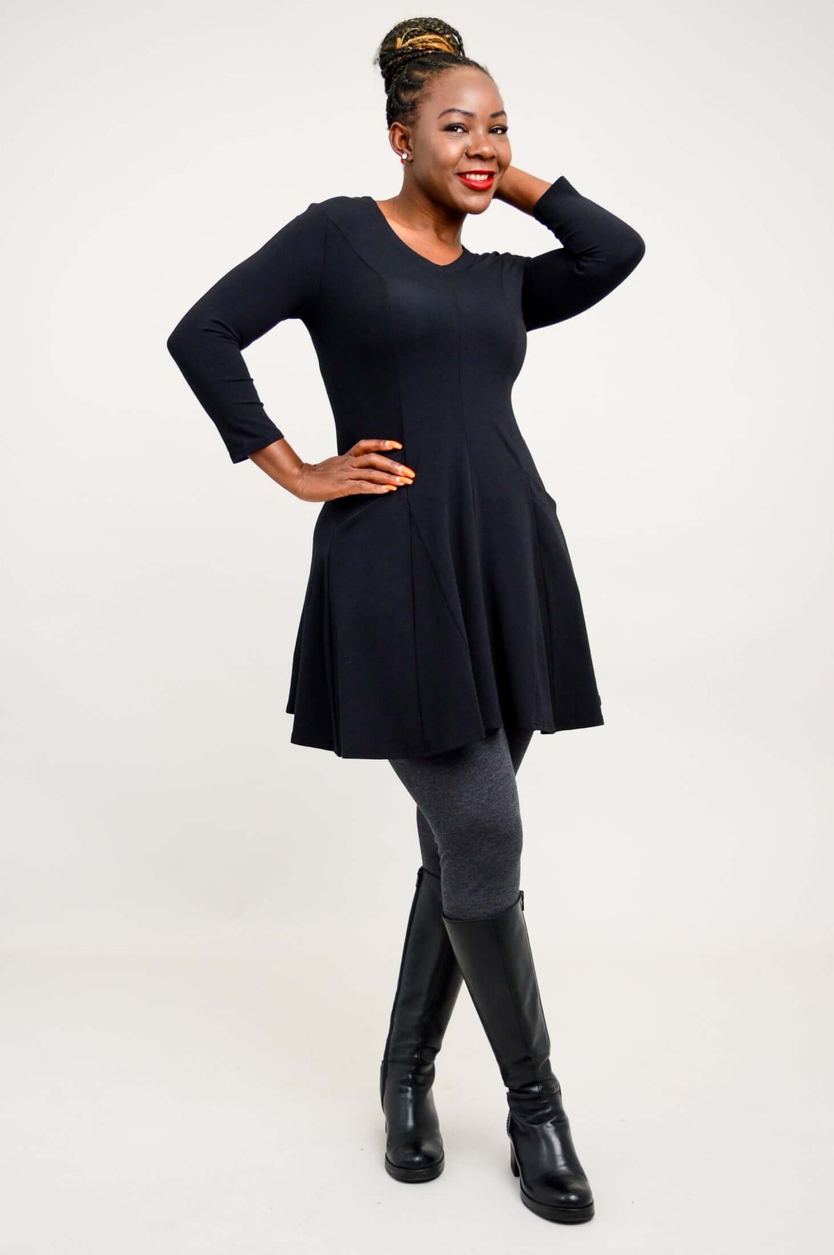 Model standing sideways with hands in pockets, wearing a black tunic dress