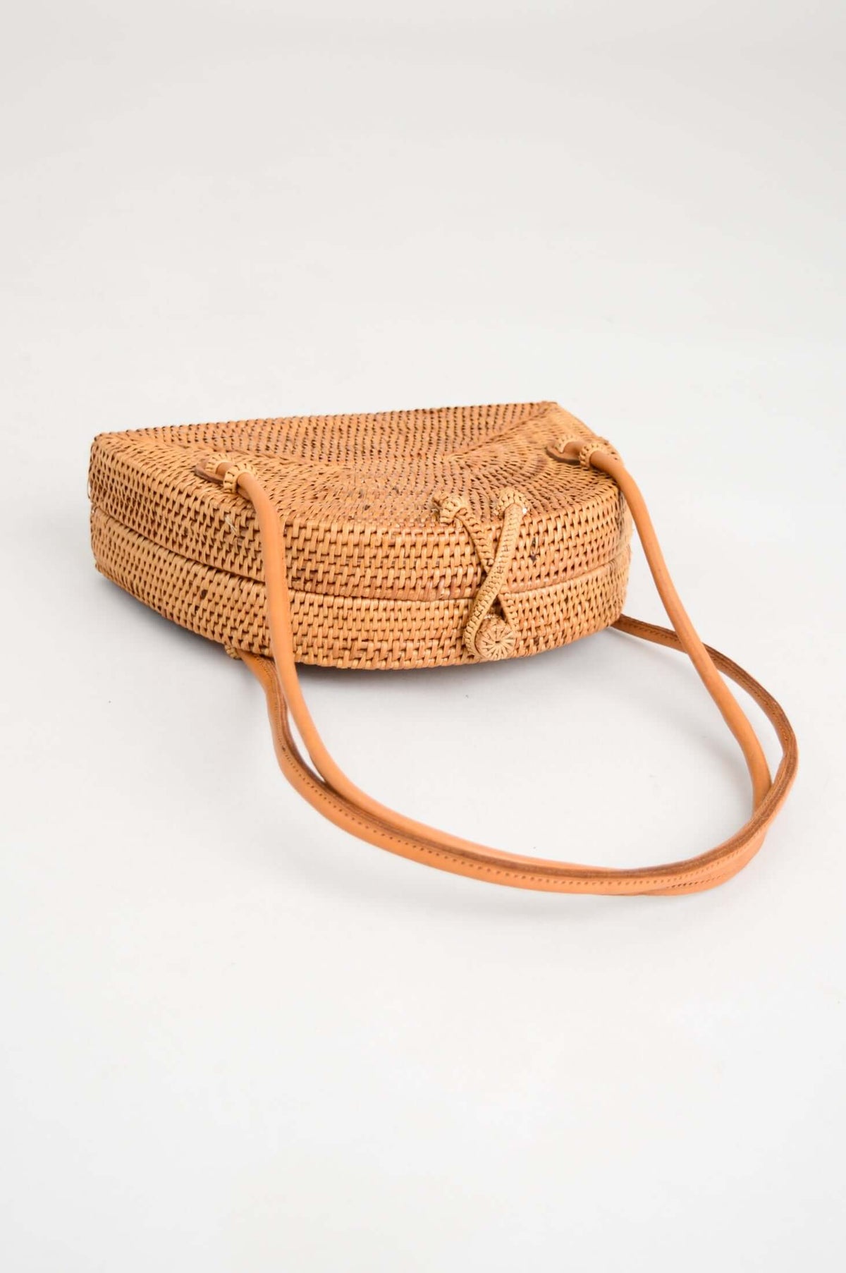 Side view of handwoven rattan bag showing flat base and leather straps