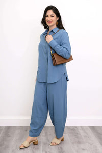 Side view of woman in sky blue shirt and pants with brown shoulder bag