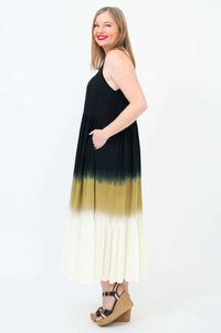 Side view of woman in a sleeveless black to golden ombre maxi dress with hand in pocket