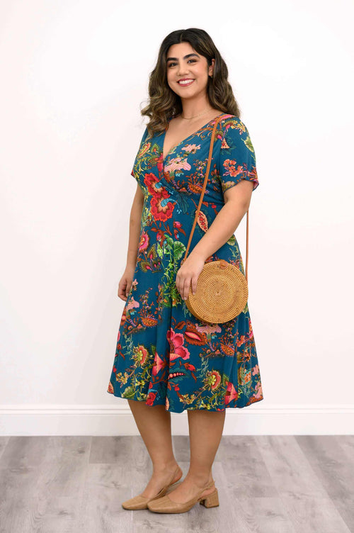 Side view of a woman in a teal floral bamboo wrap dress holding a round straw bag