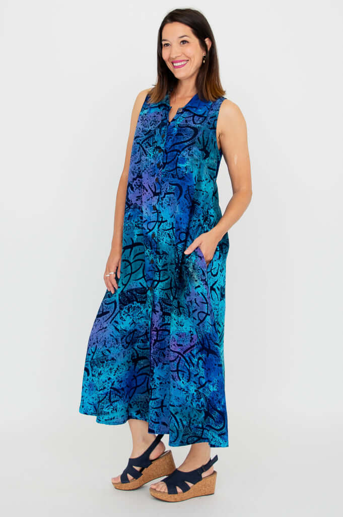 Side angle of a woman in a bright blue and purple collared A-line dress with hands in pockets
