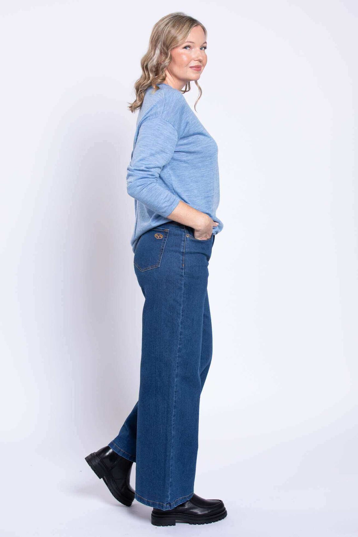 Side view of woman in wide leg blue jeans, blue sweater, and black boots
