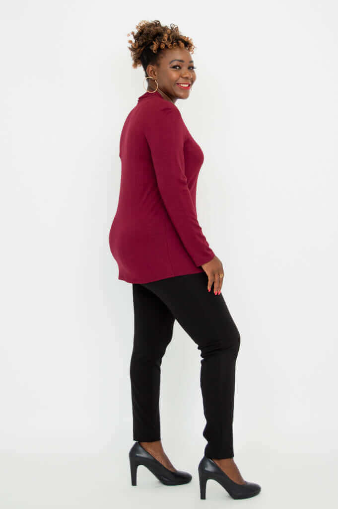 Side view of a woman in a burgundy long sleeve top paired with black pants and heels