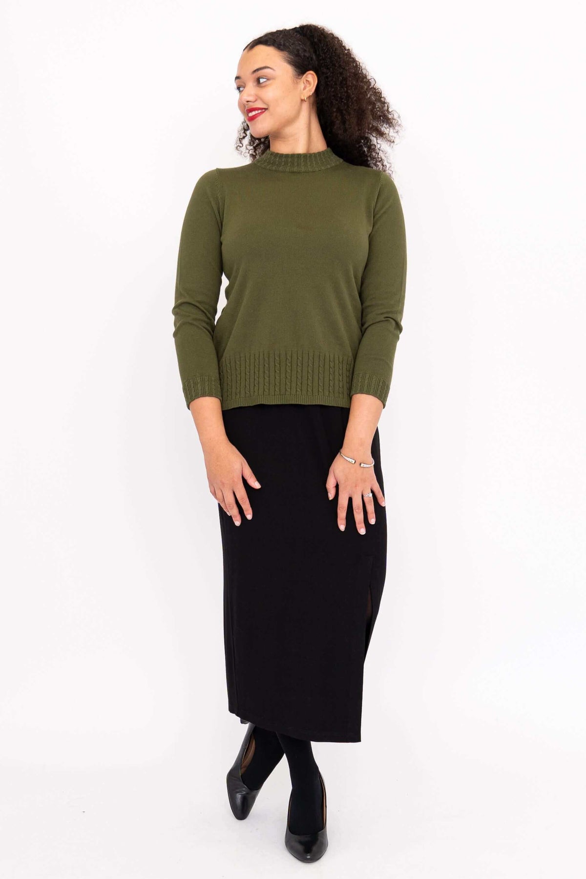 Woman turning sideways wearing an olive green sweater and black skirt