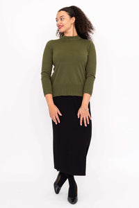 Woman turning sideways wearing an olive green sweater and black skirt