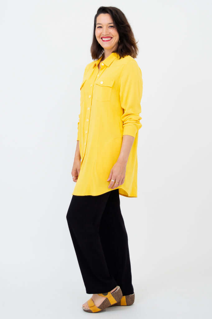Side view of woman in yellow button-up shirt tunic paired with black pants
