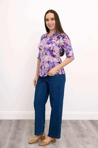 Woman posing sideways in purple and pink floral blouse with blue jeans