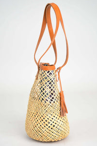 Side view of woven rattan basket tote with brown leather strap and tassel