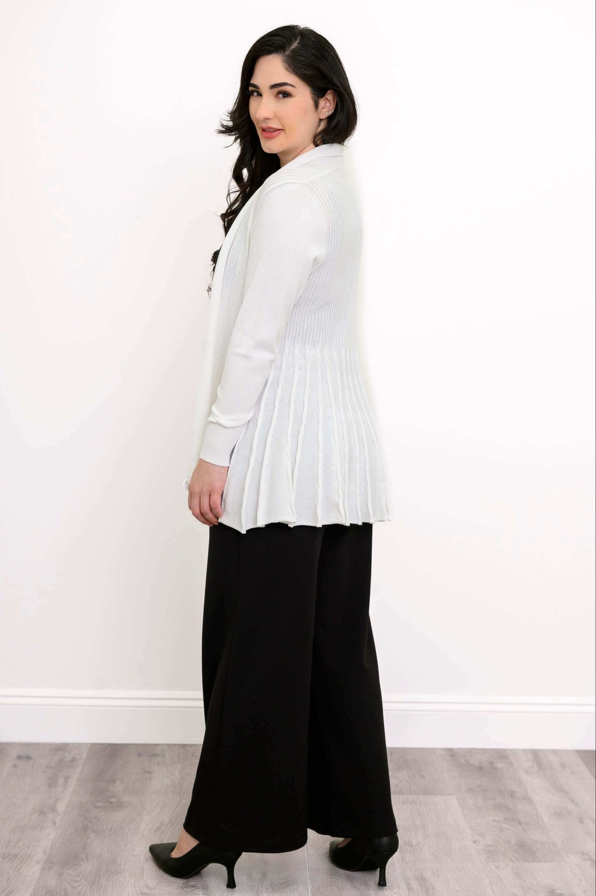 Rear side view of a woman in a white cardigan showing back pleats with black pants