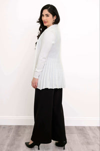 Rear side view of a woman in a white cardigan showing back pleats with black pants