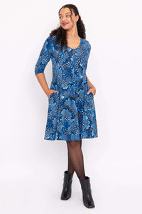 Smiling woman looking sideways, wearing a blue floral dress with pockets and black boots