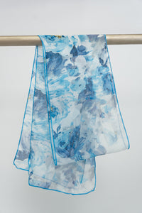 A large silk scarf with a floral pattern in shades of blue and white, displayed on a rod, front view