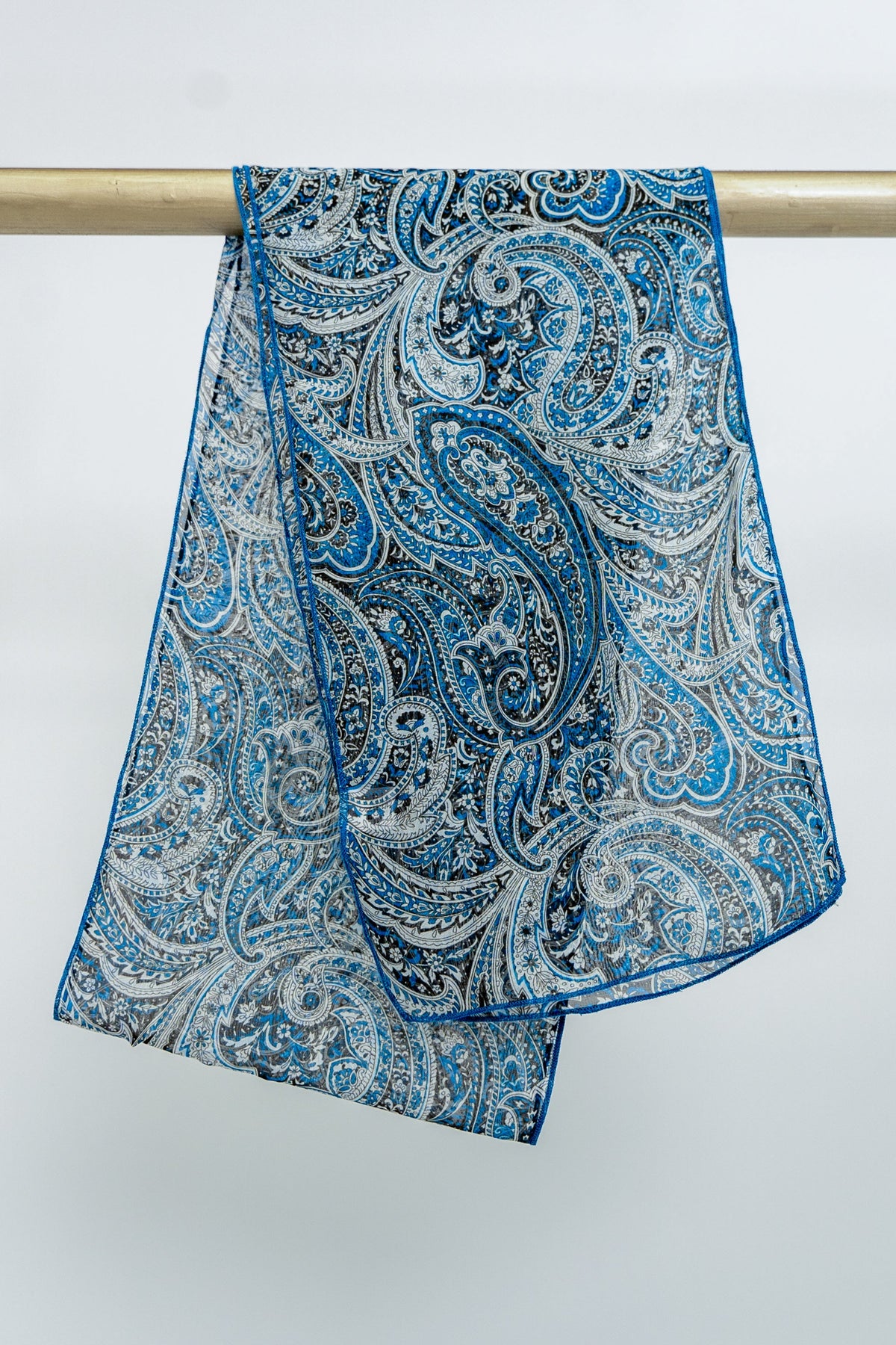 A blue and white paisley patterned silk scarf draped over a metallic rod, front view