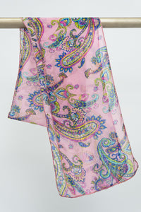 A large pink silk scarf with a yellow and blue paisley pattern, displayed on a rod against a white background, front view