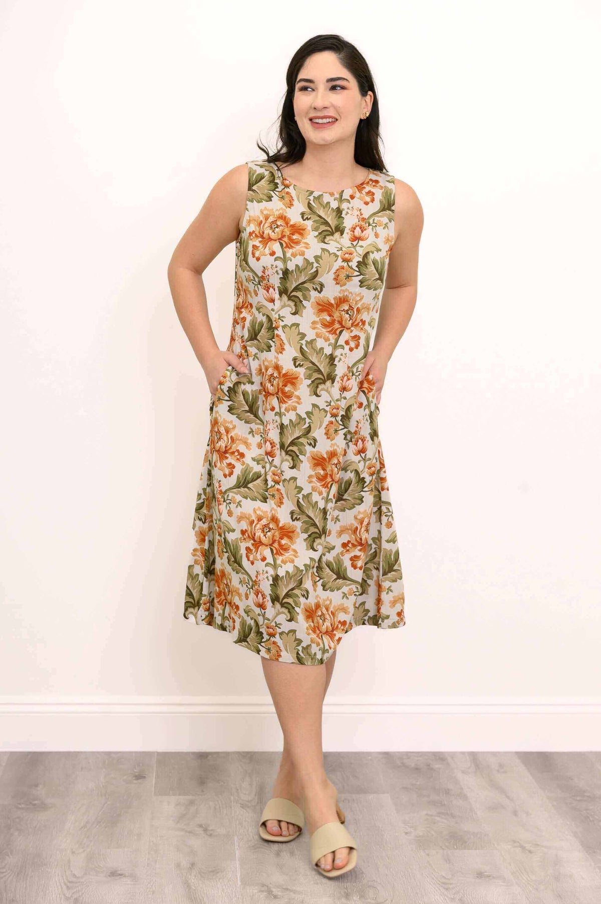 Woman in sleeveless floral dress with hands in pockets, smiling and looking away