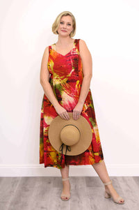 Woman in vibrant sleeveless midi dress holding straw hat, facing forward