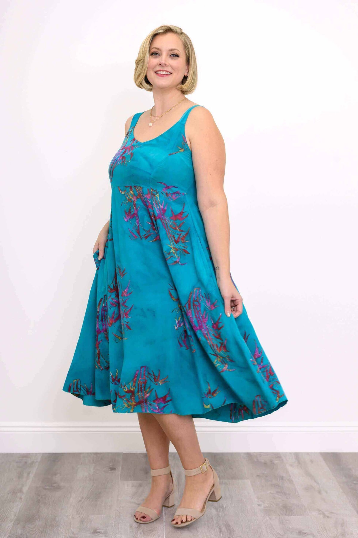 Woman wearing a sleeveless aqua blue midi dress with vibrant floral accents, smiling