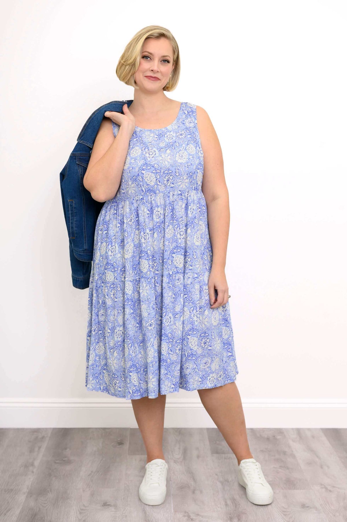 Woman in a sleeveless blue floral Juni Dress holding a denim jacket on her shoulder
