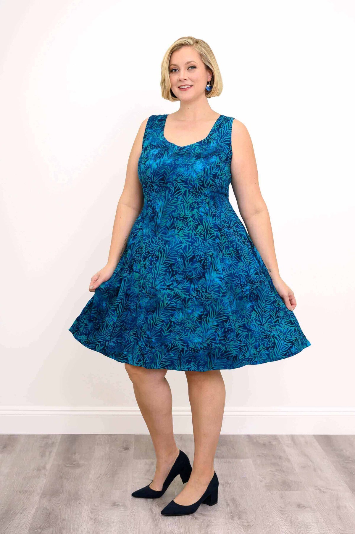 Woman posing in blue sleeveless dress with leafy pattern and heels