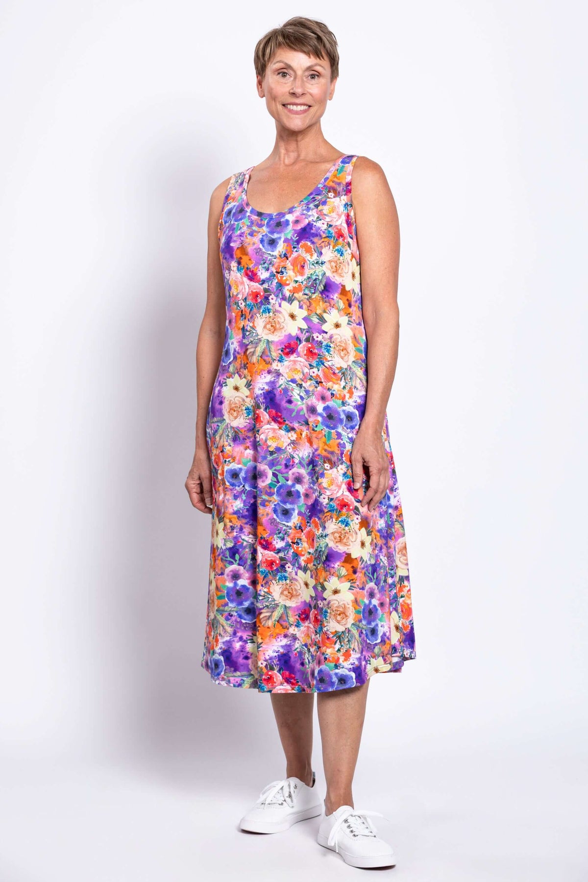 Woman smiling in a sleeveless, floral print dress with bright purple and orange flowers
