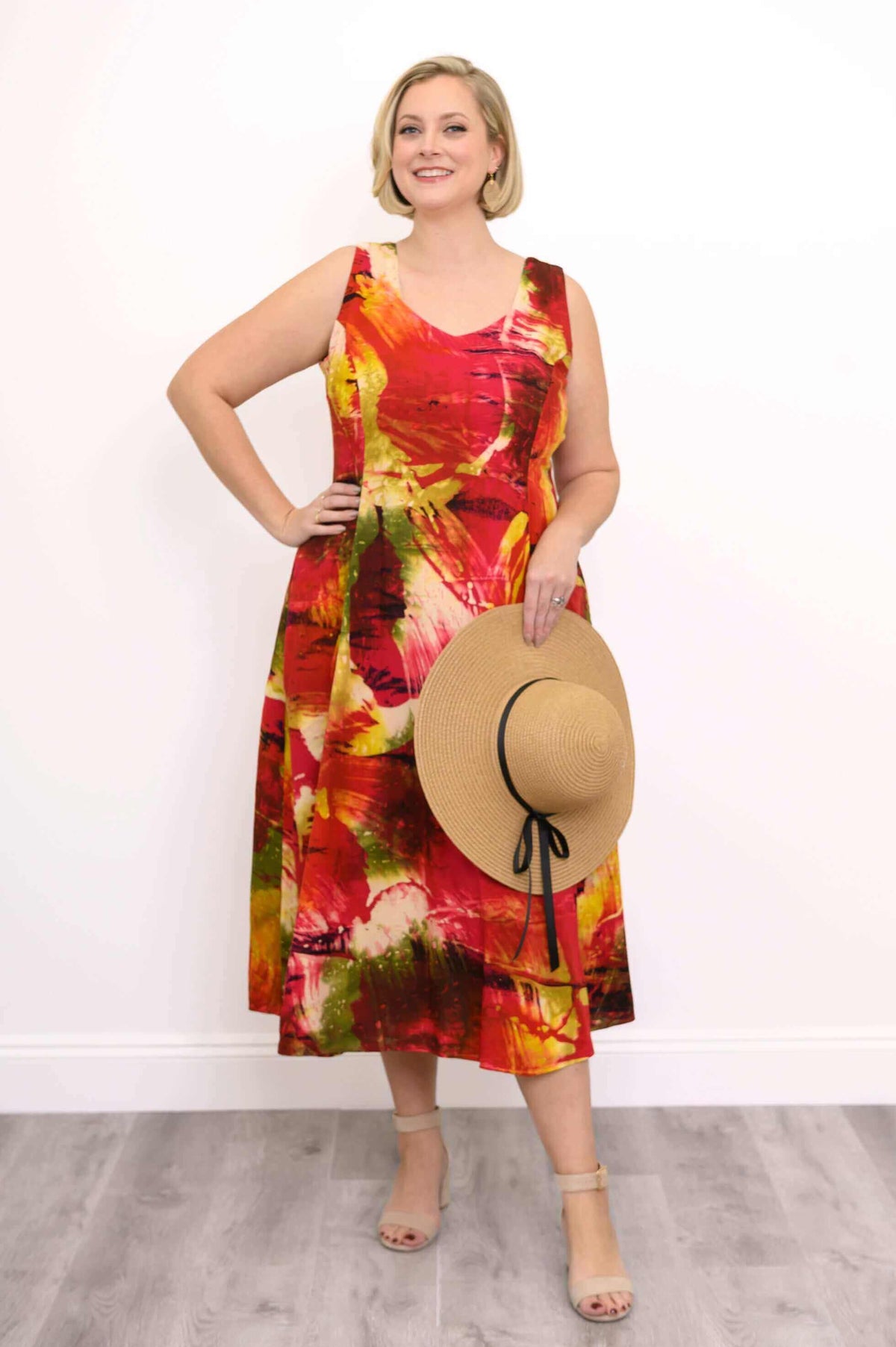 Woman wearing a sleeveless midi dress with a vibrant sunset-inspired abstract print holding a sunhat