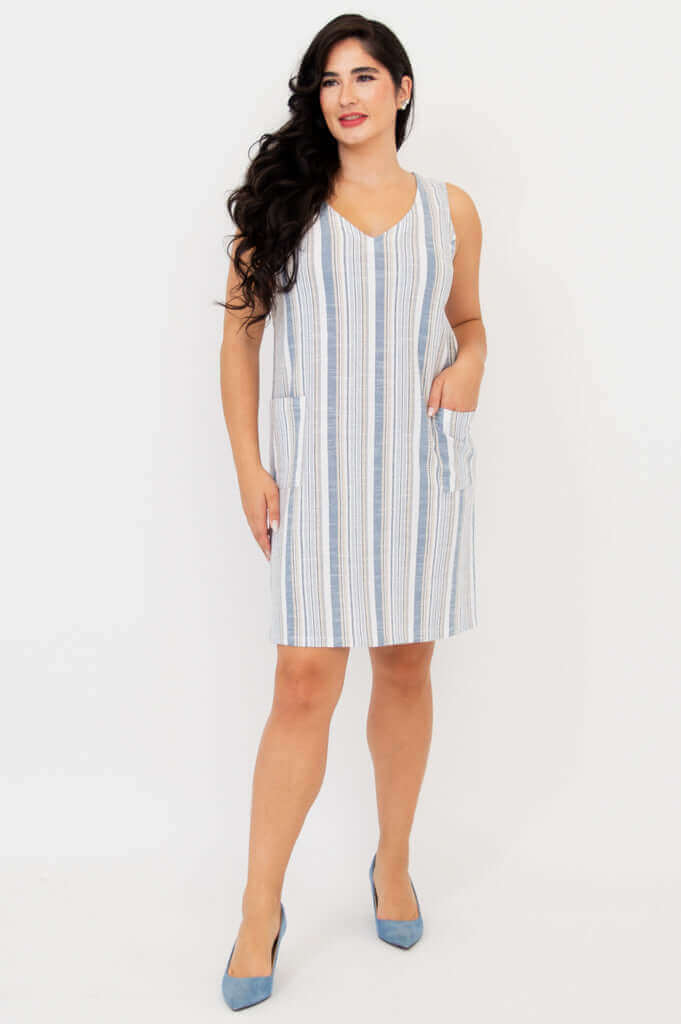 Woman modeling a sleeveless striped shift dress with front pockets and blue shoes