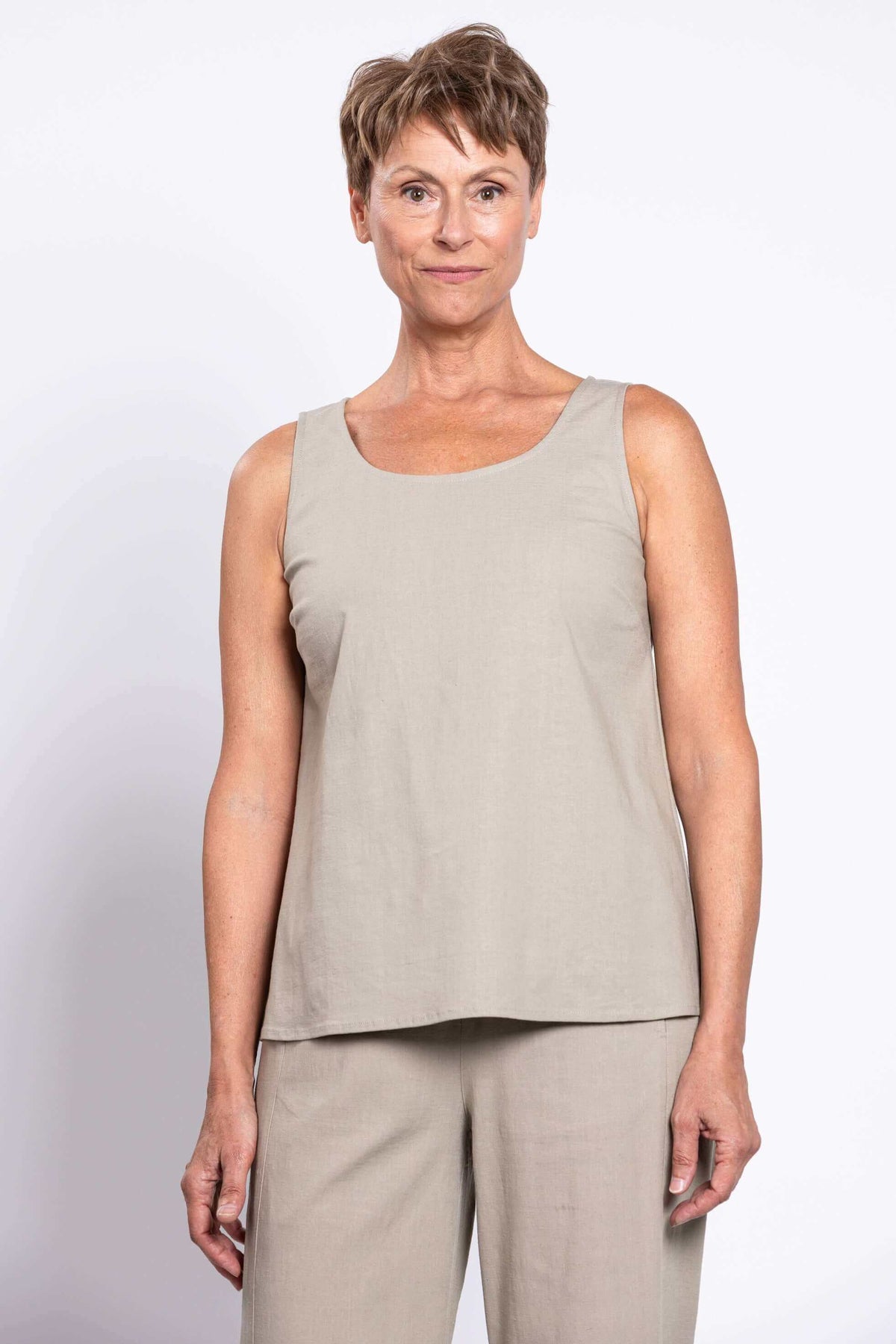 Woman wearing a sleeveless taupe A-line tank top with round neck, front view