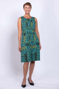 Woman wearing a sleeveless teal and yellow patterned dress, standing and smiling