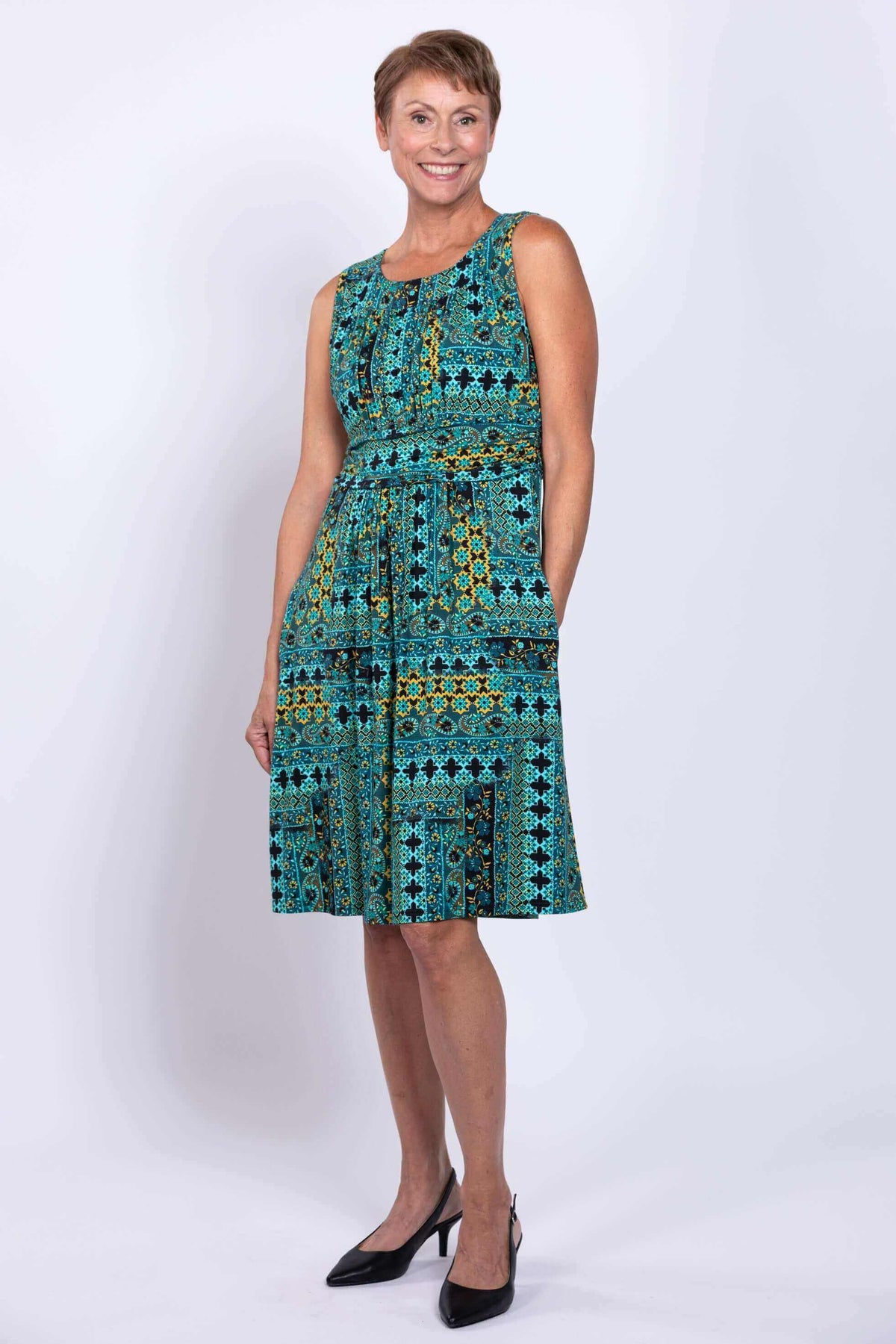 Woman posing in a sleeveless teal and yellow patterned dress, hand in pocket