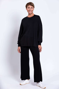 Model in black crew neck top and pants, slight pose with visible shoes