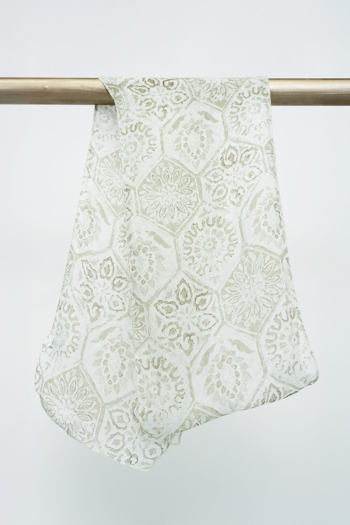 A large silk scarf with a beige geometric mosaic pattern displayed on a rod against a white background, front view