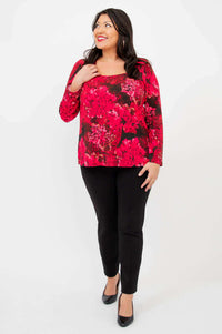 Model smiling in Marissa Crimson Bloom tunic and black pants, hand on collar