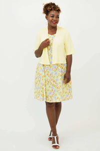 Woman smiling in cropped light yellow jacket over a floral dress, front view