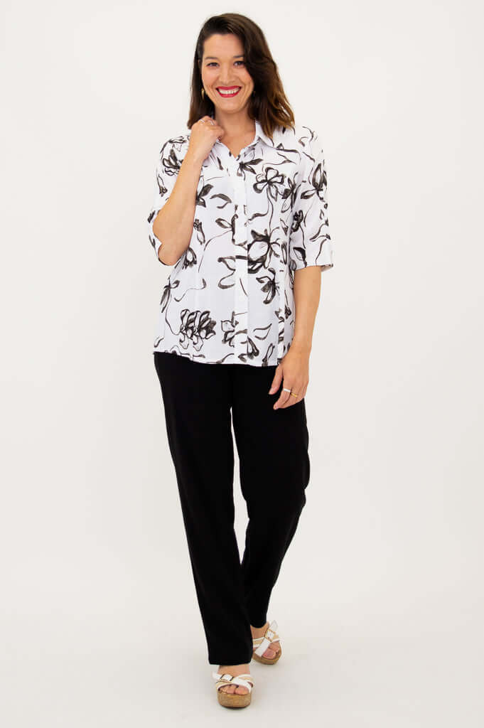 Woman smiling in white bamboo linen blouse with black artistic print and black pants
