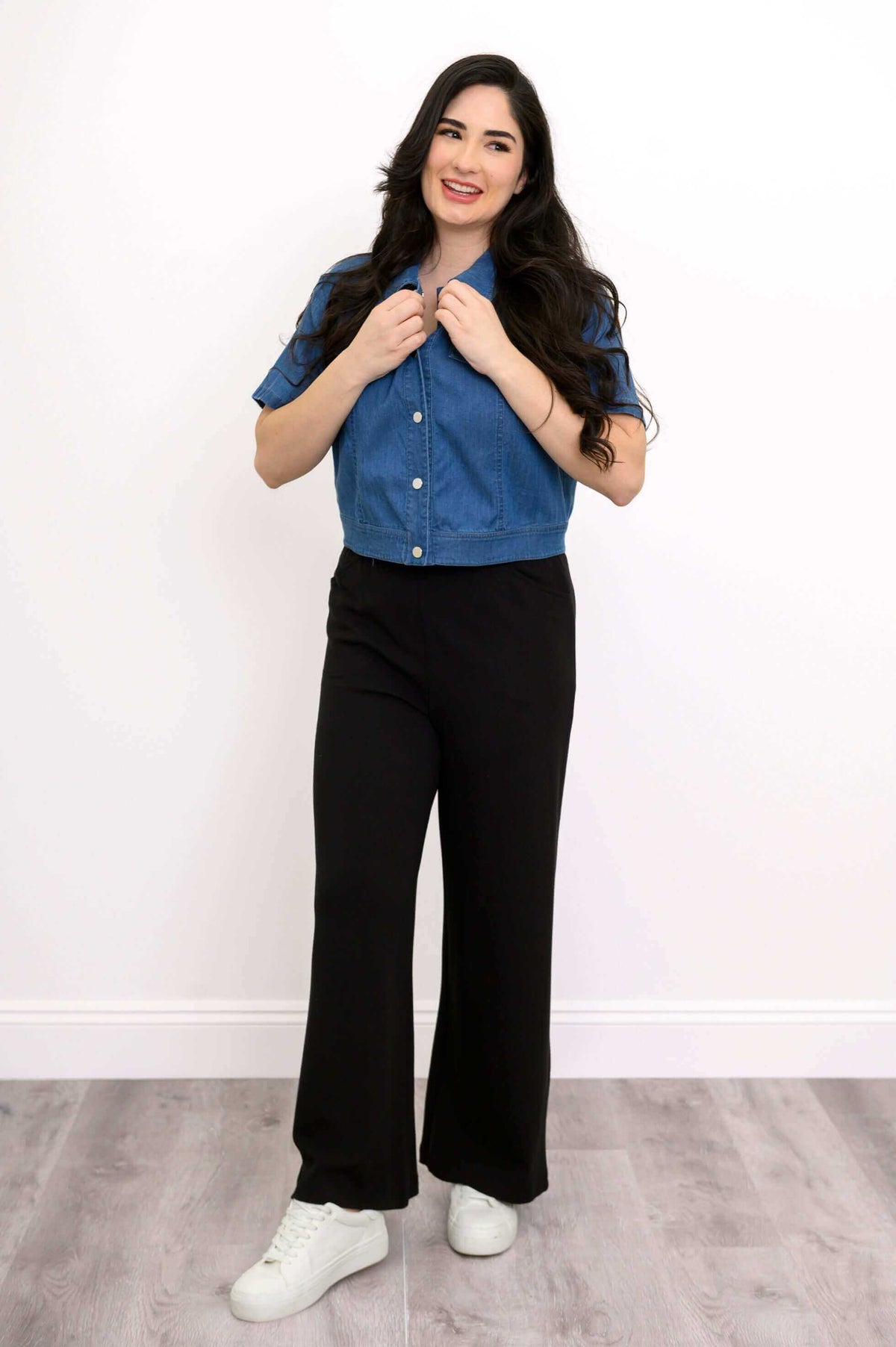 Woman smiling in blue cropped denim jacket and black pants facing forward