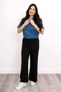 Woman smiling in blue cropped denim jacket and black pants facing forward