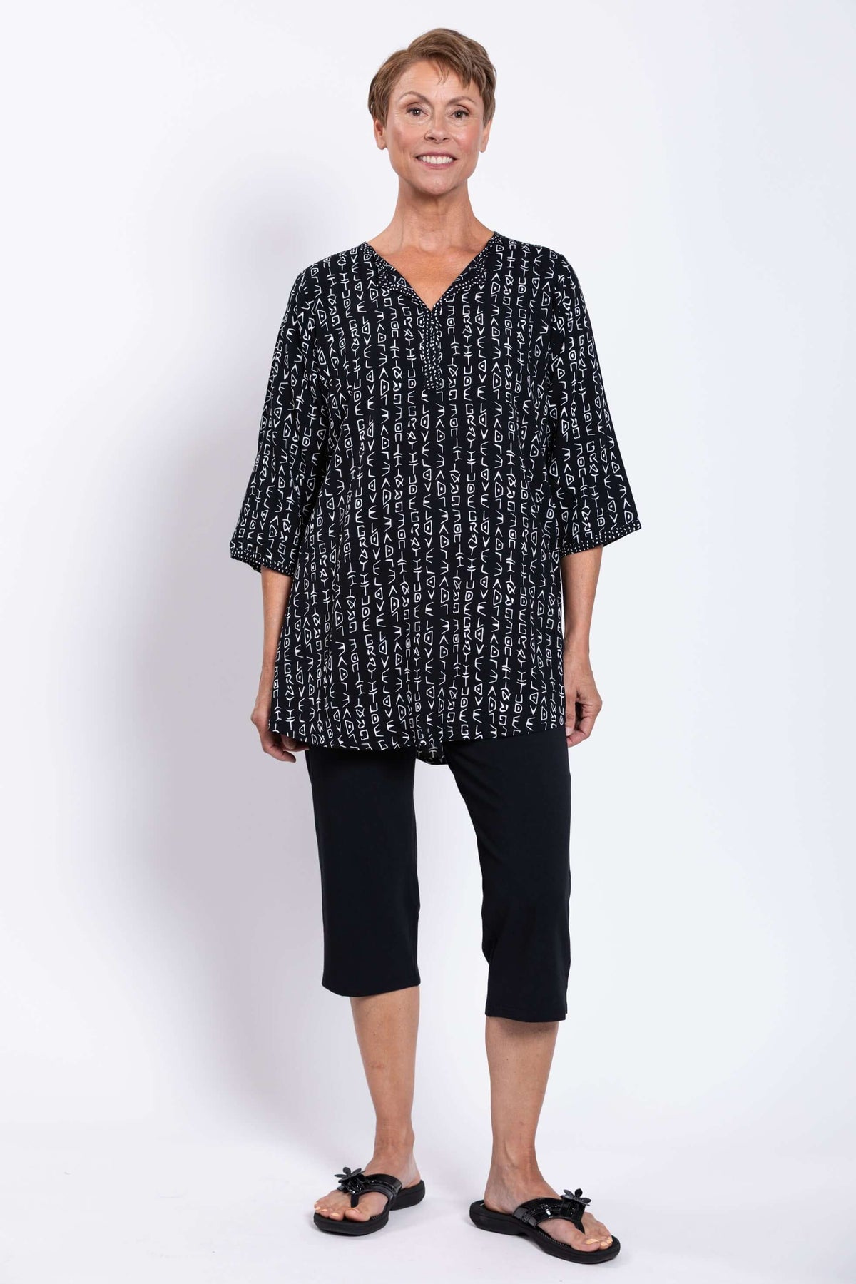Woman smiling in a black Batik blouse with white abstract print, standing upright