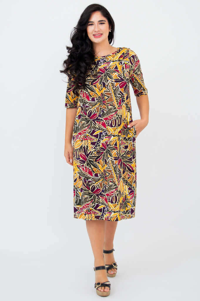 Woman smiling, wearing Olivia dress in Tropikal print, hands in pockets, facing forward