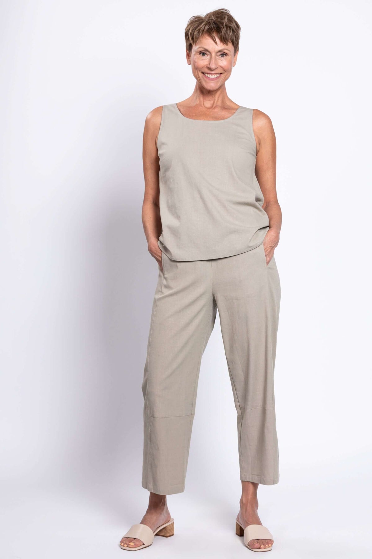 Woman smiling in a beige sleeveless tank top and matching cropped pants, hands in pockets