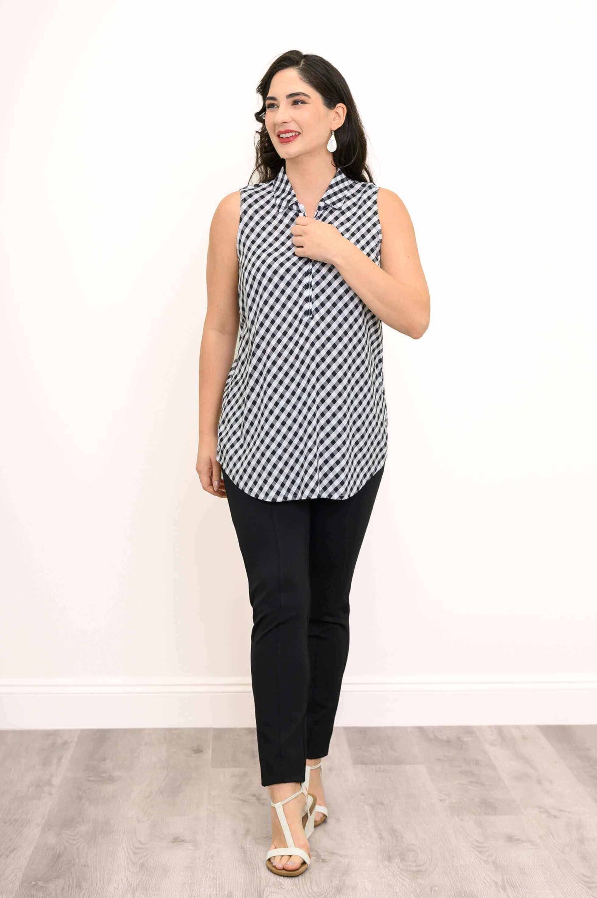 Woman in a black and white gingham tank top smiling and walking, paired with black pants and wedge sandals